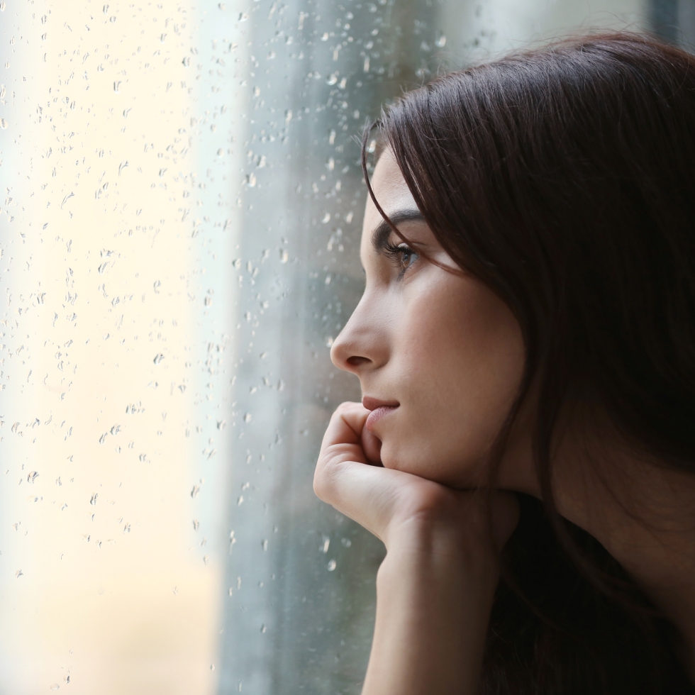 Nainen katselee mietteissään ulos sateisesta ikkunasta.