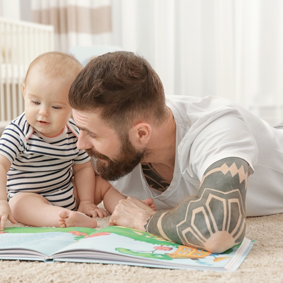 Isä ja vauva lattialla katsomassa kuvakirjaa.