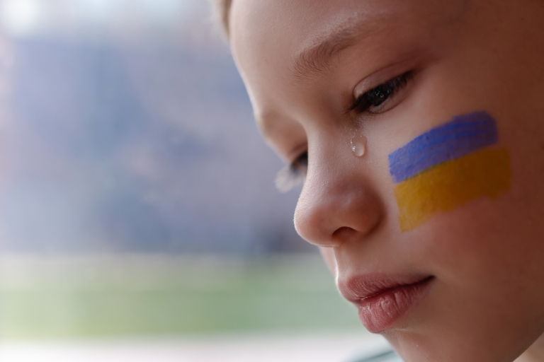Surullinen pieni poika, kyynel silmässä katselee alaspäin. Ukrainan lippu on maalattu poskeen. 