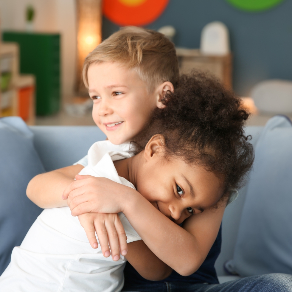 Kaksi pientä lasta halaa toisiaan ehkä päiväkodin sohvalla.