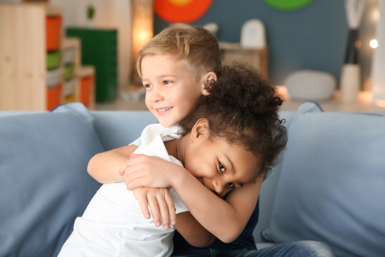 Kaksi pientä lasta halaa toisiaan ehkä päiväkodin sohvalla. 