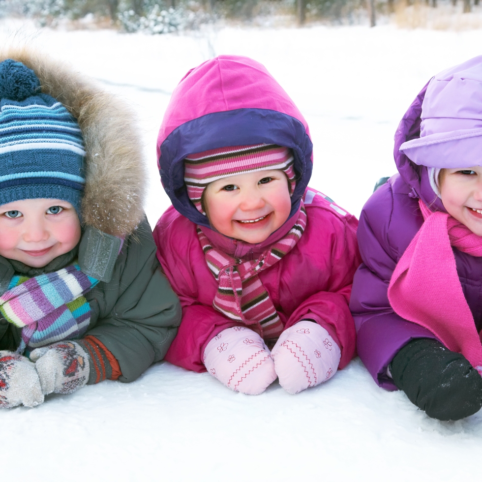 Kolme lasta makaa lumihangessa.